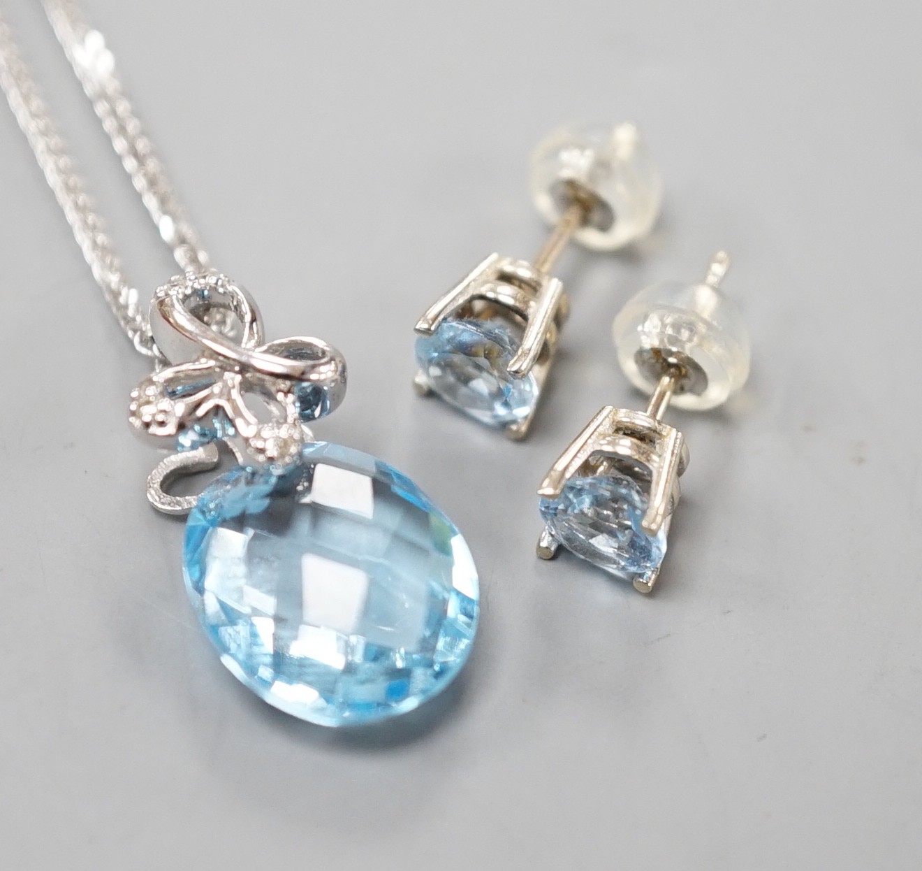 A modern 14k white metal, facetted pear cut blue topaz and diamond chip set pendant, 19mm, on a 750 white metal chain, 44cm and a pair 14k and blue topaz ear studs, gross weight 5.1 grams.